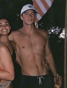 a man and woman standing next to each other in front of an american flag on the beach