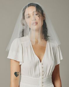 a woman wearing a white wedding dress with a veil over her head and tattoos on her arm