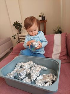 a toddler playing with tin foil in a play tray on the couch at home