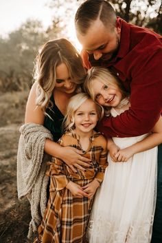 a family hugging each other in the middle of an open field with trees behind them