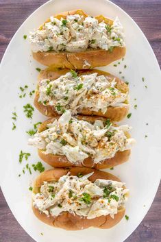 three hot dogs with chicken salad on buns sitting on a white plate, ready to be eaten