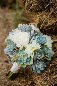 a bridal bouquet with succulents and white flowers on the ground in front of straw bales