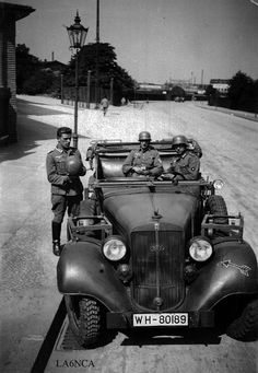 two men in uniforms standing next to an old fashioned car on the side of a road