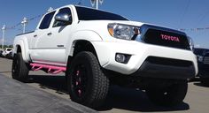 a white toyota truck with pink rims parked in a parking lot next to other vehicles