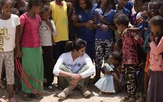 a woman kneeling down in front of a group of children