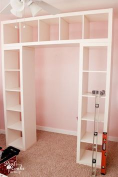 a room with pink walls and white shelving unit in the corner, along with a ceiling fan