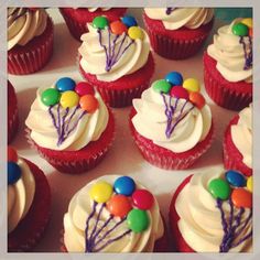 cupcakes with white frosting and colorful balloons on top are arranged in rows