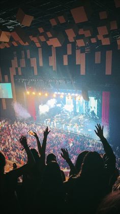 an audience at a concert with their hands in the air and lights shining down on them