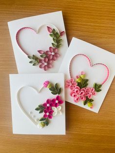 three cards with flowers and hearts on them sitting next to each other in front of a wooden table