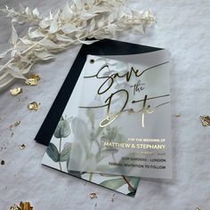 wedding save the date cards with gold confetti and leaves on white paper next to streamers