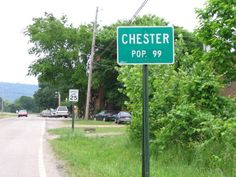 a green street sign sitting on the side of a road next to a lush green forest