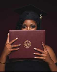 a woman in graduation cap and gown holding up a red book with gold lettering on it