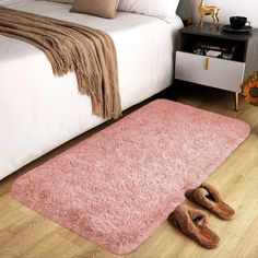 a pink rug on the floor in front of a bed with two slippers next to it