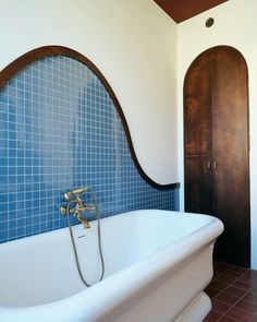 a bath tub sitting next to a wooden door in a room with blue tiles on the walls