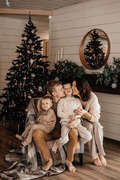 a mother and her two children sitting on a chair in front of a christmas tree