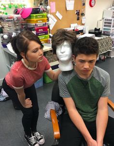 two young people sitting in chairs with mannequins behind them