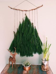 a small deer statue next to a fake christmas tree hanging from a rope on a wall