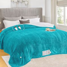 a bed covered in a teal colored blanket and pillows with headphones on it