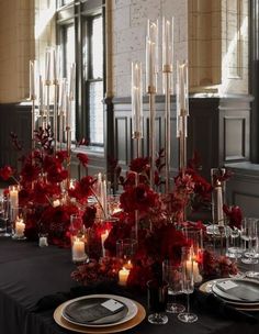 a table is set with candles, plates and vases filled with red flower arrangements