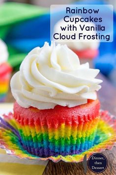 a cupcake with white frosting and rainbow icing on a colorful paper plate