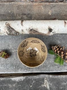 a brown bowl sitting on top of a wooden table next to pine cones and needles