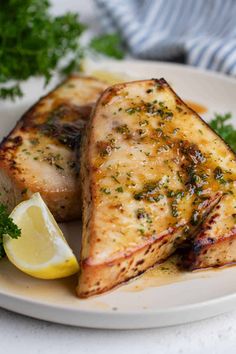 two pieces of fish on a white plate with lemon wedges and parsley next to it