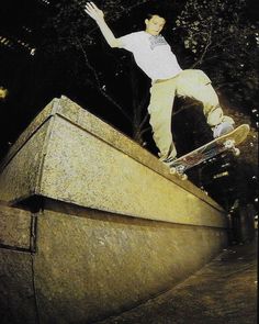 a man riding a skateboard up the side of a cement wall at night with trees in the background