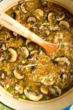 a pot filled with mushrooms and green peas next to a wooden spoon on top of a table