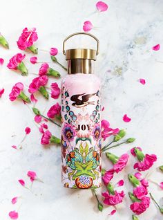 a pink water bottle sitting on top of a marble counter next to flowers and leaves