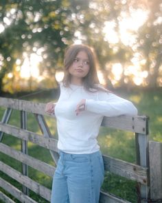 a woman leaning on a wooden fence posing for the camera