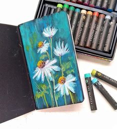 an art journal with crayons and pastels next to it on a table