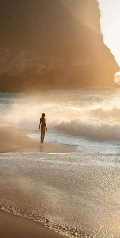 a person walking on the beach in front of the ocean with waves crashing against them