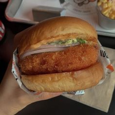 a person holding a chicken sandwich in front of a bowl of macaroni and cheese