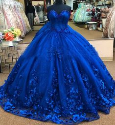 Embrace the magic of your quinceanera with this exquisite royal blue ball gown. The dramatic ball gown is crafted from luxurious tulle, and offers a voluminous, fairy-tale look, while the chapel train adds a regal flair, perfect for your grand entrance. The strapless neckline creates an elegant and timeless look, highlighting your shoulders and neckline with sophistication. What truly sets this gown apart are the stunning 3D flowers and applique detailing, which delicately adorn the bodice and s Floral Quince Dress, Royal Blue Princess Dress, Royal Blue Quince Dress, Floral Quince, Blue Quince Dress, Royal Blue Ball Gown, Royal Blue Quinceanera Dresses, Royal Blue Quince, Royal Blue Quinceanera