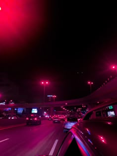 cars driving down the road at night with red lights in the dark sky above them