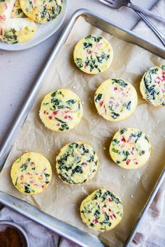 several muffins with spinach and cheese are on a baking sheet next to a bowl of sauce