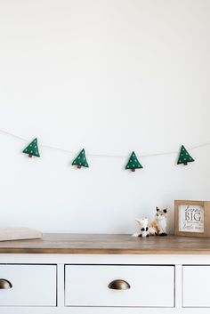 a dog sitting on top of a wooden table next to a white dresser with green christmas trees