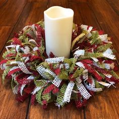 a white candle sitting on top of a wooden floor next to a christmas mesh wreath