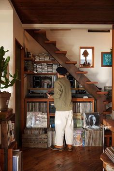 a man standing in front of a book shelf filled with books and vinyl records next to a stair case