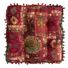 a red and green patchwork pillow with pom - poms on the bottom