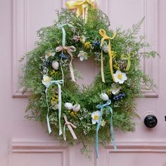 a wreath with flowers and ribbons hanging on a door