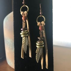 two pairs of earrings with beads and feathers hanging from it's ear hooks on a black display stand