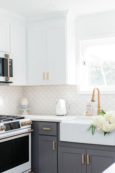 a kitchen with white and gray cabinets, an oven, sink, microwave and flowers on the counter