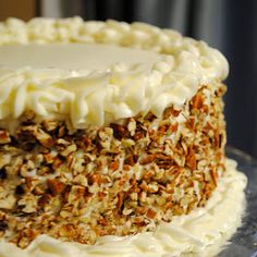 a close up of a cake with white frosting and chopped nuts on the top