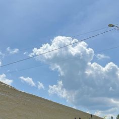 some people are standing on the side of a hill under a blue sky with white clouds