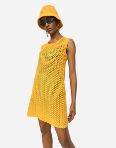 a woman in a yellow knitted dress and sun hat poses for the camera with her hands on her hips