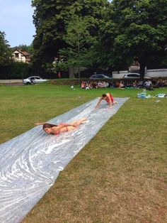 two women laying on a tarp in the grass with people watching from behind them