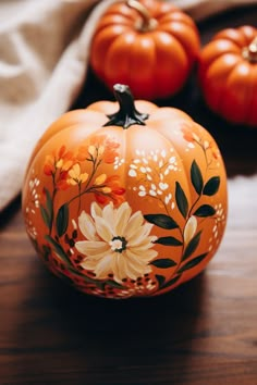 an orange painted pumpkin sitting on top of a wooden table next to other pumpkins