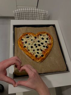 a person making a heart shaped pizza with olives and cheese on it in a box