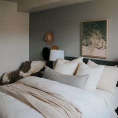 a bed with white linens and pillows in a bedroom next to a painting on the wall